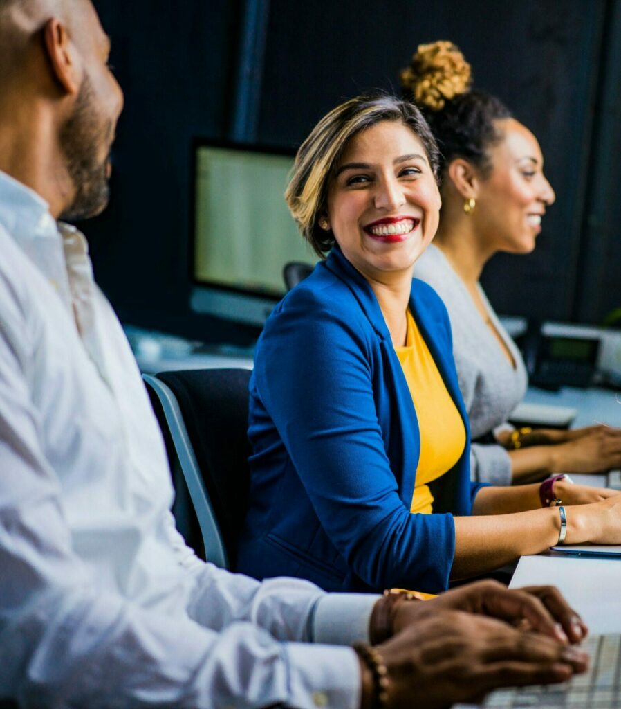 A woman smiling at a man while they both type on keyboards in an office